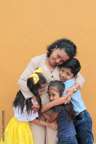 Young, 50-year-old Latina grandmother with brown skin takes care of her grandson and granddaughters, who show their love with hugs to celebrate Mother's Day