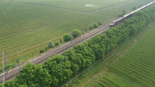 Aerial view of a high-speed red train racing across Italian vineyards, blending modern transportation with timeless landscapes.