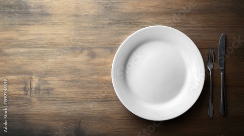 Empty white ceramic plate with fork and knife on a rustic wooden table, overhead view conveying minimalist simplicity and quiet anticipation before a meal