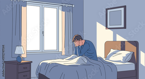 Stressed young man sitting on his bed with his head in his hands during the morning with sunlight coming through the window.