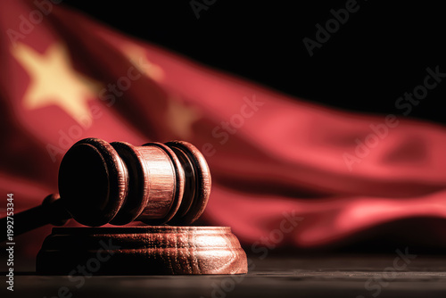 A wooden judge's gavel resting on its sound block against a blurred Chinese national flag, set against a dark background, symbolizing Chinese law and justice.