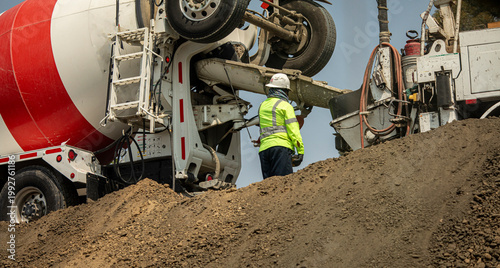 Fotografie Looking up at a construction worker near a cement truck delivering cement