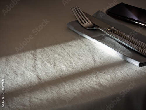 Shiny silver cutlery placed neatly on a grey linen napkin resting upon a white dinner table