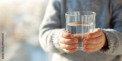 Close up of young child hands holding glass of clear water, showcasing innocence and purity in bright setting