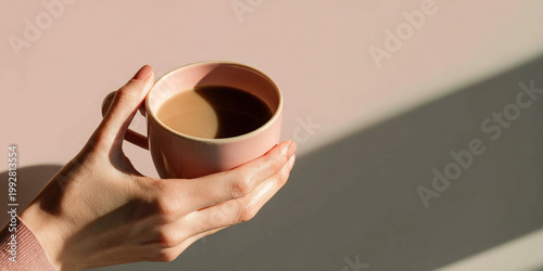 Aesthetic female hand holding pink coffee cup, showcasing minimalism and warmth in soft light