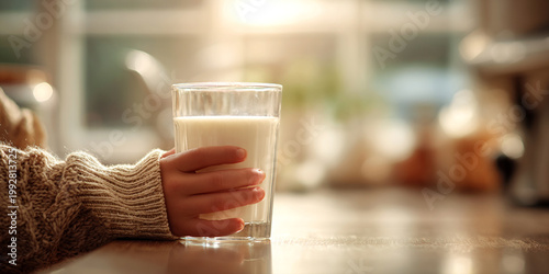 Child hand gently holds glass of milk, creating warm and inviting atmosphere cozy kitchen. soft light enhances moment