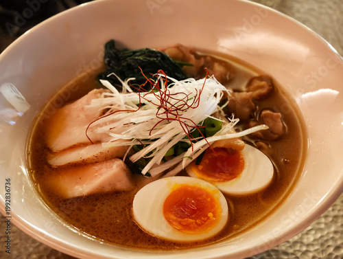 High-angle of a bowl of Japanese ramen with chashu, soft-boiled egg, and scallion strips