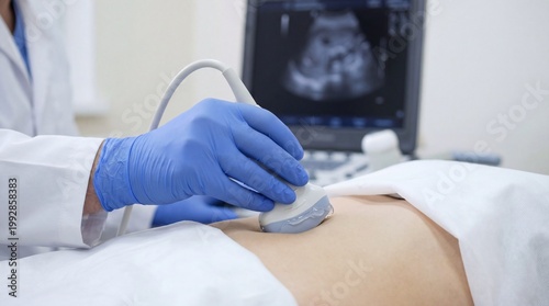 Medical professional in white coat using ultrasound device on pregnant woman's abdomen during examination in a clinical setting with monitor displaying ultrasound image