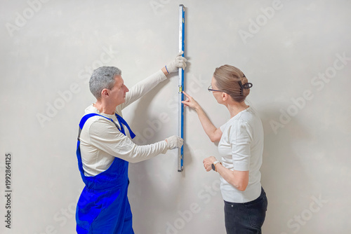 Man and woman measure wall together.