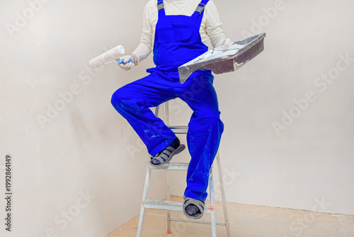 Unrecognizable worker in bright blue overalls sits on ladder