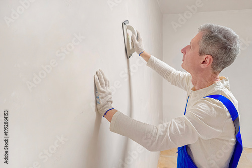 Man applies plaster to smooth wall with trowel