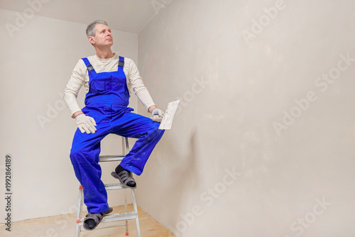 Man in blue overalls sits on ladder