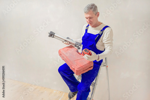 Worker sits on ladder holding laser level for construction and finishing works.