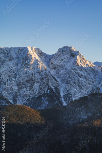 Snow-covered mountains rise against a clear blue sky during early morning sunlight in a remote wilderness area. Giewont, Tatra mountains, Zakopane, Poland