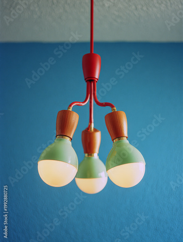 Modern red chandelier with three green and wooden light bulbs hanging against blue wall, creating warm and cozy atmosphere