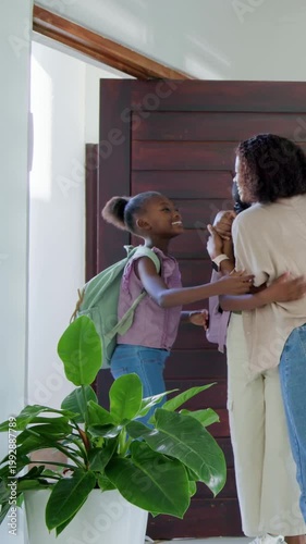 Vertical video: Returning to wooden door, mom opening and guiding child in with mint-green backpack