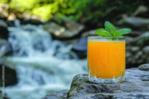 Refreshing orange juice in a glass with mint on a stone surface, against a waterfall backdrop, natural food concept