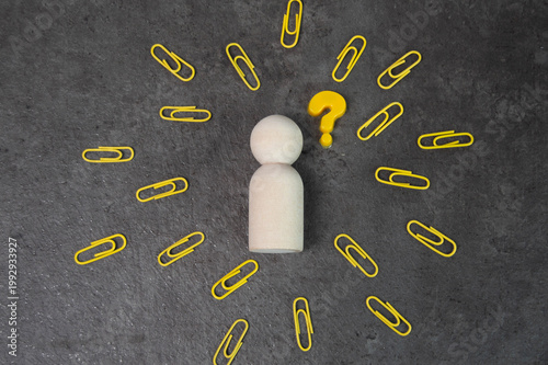 Wooden figure surrounded by paper clips and a question mark symbolizing confusion or a dilemma