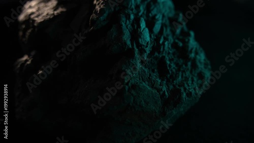 Close-up dark rock surface with green light and rugged texture