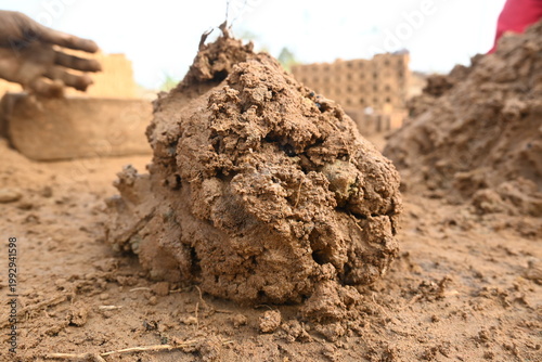 A person manually shaping bricks in an open field. Using a rectangular wooden mold and raw, reddish-brown clay, the worker skillfully forms each brick on the dusty ground. Slow motion video.