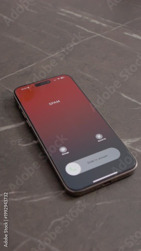 Vertical Screen: A smartphone displays an incoming call marked as spam. It rests on a table, highlighting the issue of unwanted calls and the need for detection strategies.