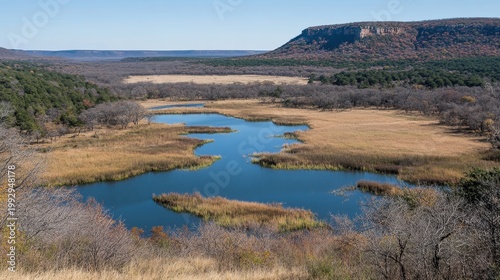 Expansive natural landscape with a winding blue water body, dry fields, and a distant plateau under a clear sky