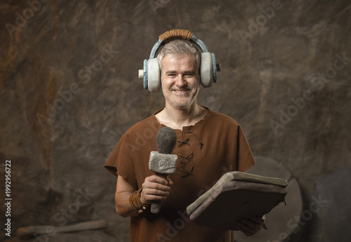 Obraz na plátně Funny Prehistoric Caveman Broadcasting with Primitive Stone Headphones and Micro
