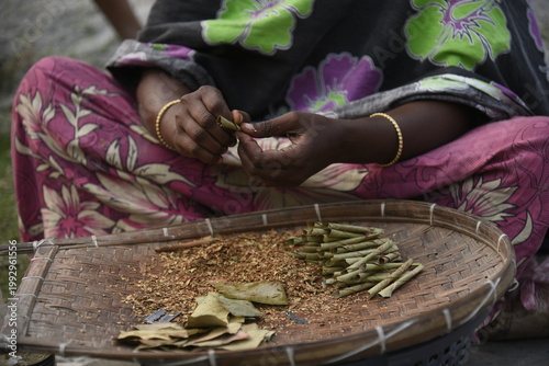 A woman prepares traditional bidi tobacco products, carefully rolling tendu leaves with processed tobacco by hand, reflecting small-scale cottage industry work, skilled craftsmanship