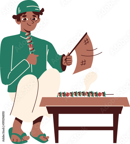 Smiling street vendor in green traditional attire fanning sizzling food skewers on a brown table pointing with decorative necklace.