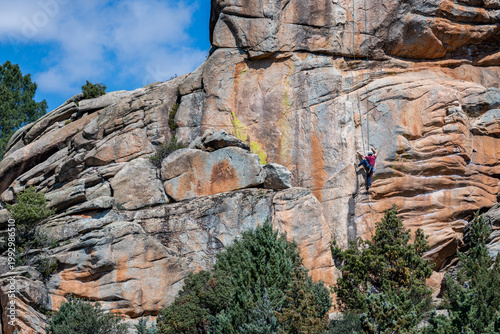 Climber on a granite rock wall in La Pedriza, with forest below and a snow-capped mountain background. A striking scene that captures adventure travel, outdoor exploration, and natural beauty of Spain