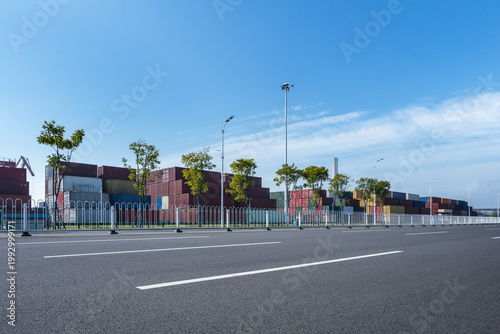 Empty Urban Roadway Bordering Container Yard Under Bright Blue Sky