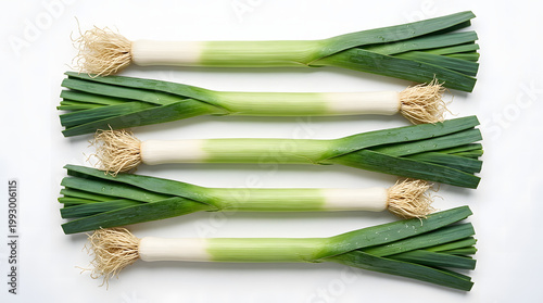 Four fresh whole leeks arranged in a parallel pattern with visible roots and vibrant green tops on white.