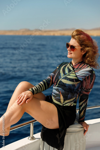 Young woman in floral swimsuit enjoying sea breeze on boat