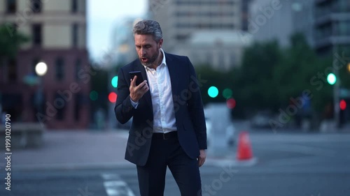 Angry businessman dealing with problem call in evening city traffic. Nervous executive speaking angrily on phone while walking downtown. Angry manager on cellphone showing stress and irritation.