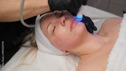 Professional beautician using a modern device for a non-invasive skin rejuvenation treatment. Blue light therapy for acne and cleansing