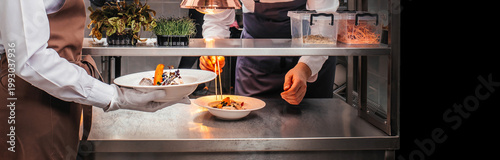 Fotografie Chef plating gourmet dish and waiter serving in professional restaurant kitchen