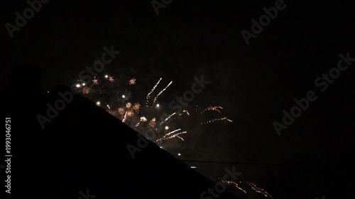 dark night sky with colorful new year party fireworks in different colors behind a black house silhouette