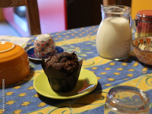 Foto Muffin al cioccolato servito su un piattino verde acido accanto a una brocca di vetro piena di latte fresco su una tavola da colazione colorata e allegra