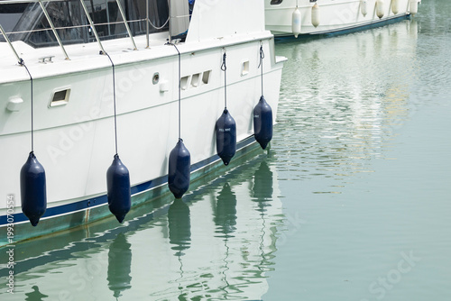 A white luxury yacht is docked at a marina, with dark blue fenders hanging along its hull