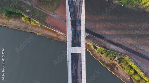 Top-down aerial drone tracking shot of a pedestrian walking across the Keel Crossing bridge in Sunderland at dawn, showcasing the modern architectural design and river landscape.