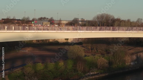 Aerial tracking shot flying sideways along the Keel Crossing pedestrian bridge in Sunderland at sunrise, showing the modern architecture and urban landscape.
