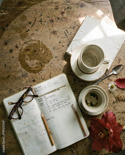 A table topped with an open notebook, a cup of tea, and a spoon, accompanied by a flower and a pair of glasses. Brain longevity morning ritual flatlay.