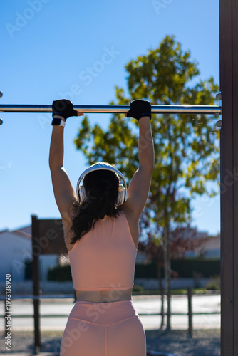 Obraz na plátně Sportswoman training back muscles with pull-ups in an outdoor gym