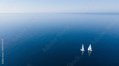 Two sailboats gliding on calm blue ocean under clear sky