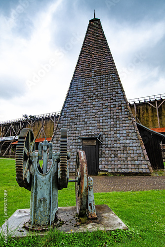 Quadro em tela Historic brine pump in the foreground with a saltworks tower and graduation tower in the background, showing traditional salt production technology in a calm landscape