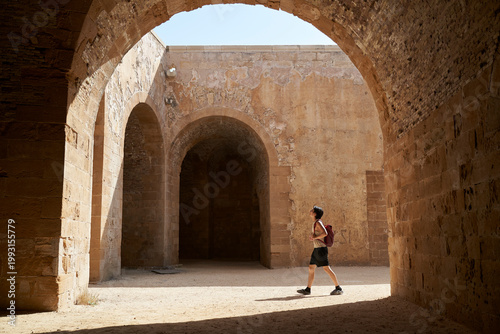 a young Asian man walking through archway of a castle in Siracusa, Sicily, Italy, during summer vacation