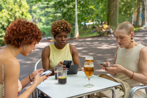 Women sitting at outdoor cafe using smartphones