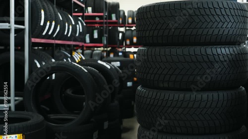 Stack of black rubber tires displayed in a tire shop with shelves filled with additional tires in the background, showcasing various tread patterns and sizes