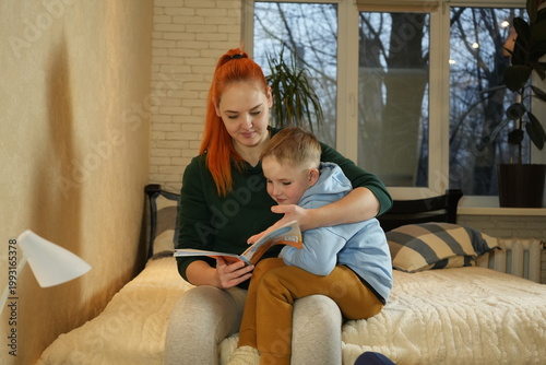 Mother reading a book with her young son at home. Warm family moment, parenting, child education and early learning concept.