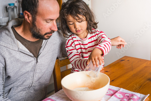 father daughter baking together at home in the kitchen making dough, concept of fatherhood and bonding with children, cooking together with complicity
